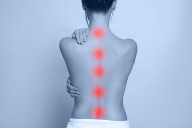 Woman suffering from back pain on light background