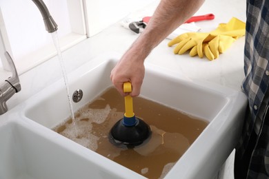 Photo of Man using plunger to unclog sink drain in kitchen, closeup
