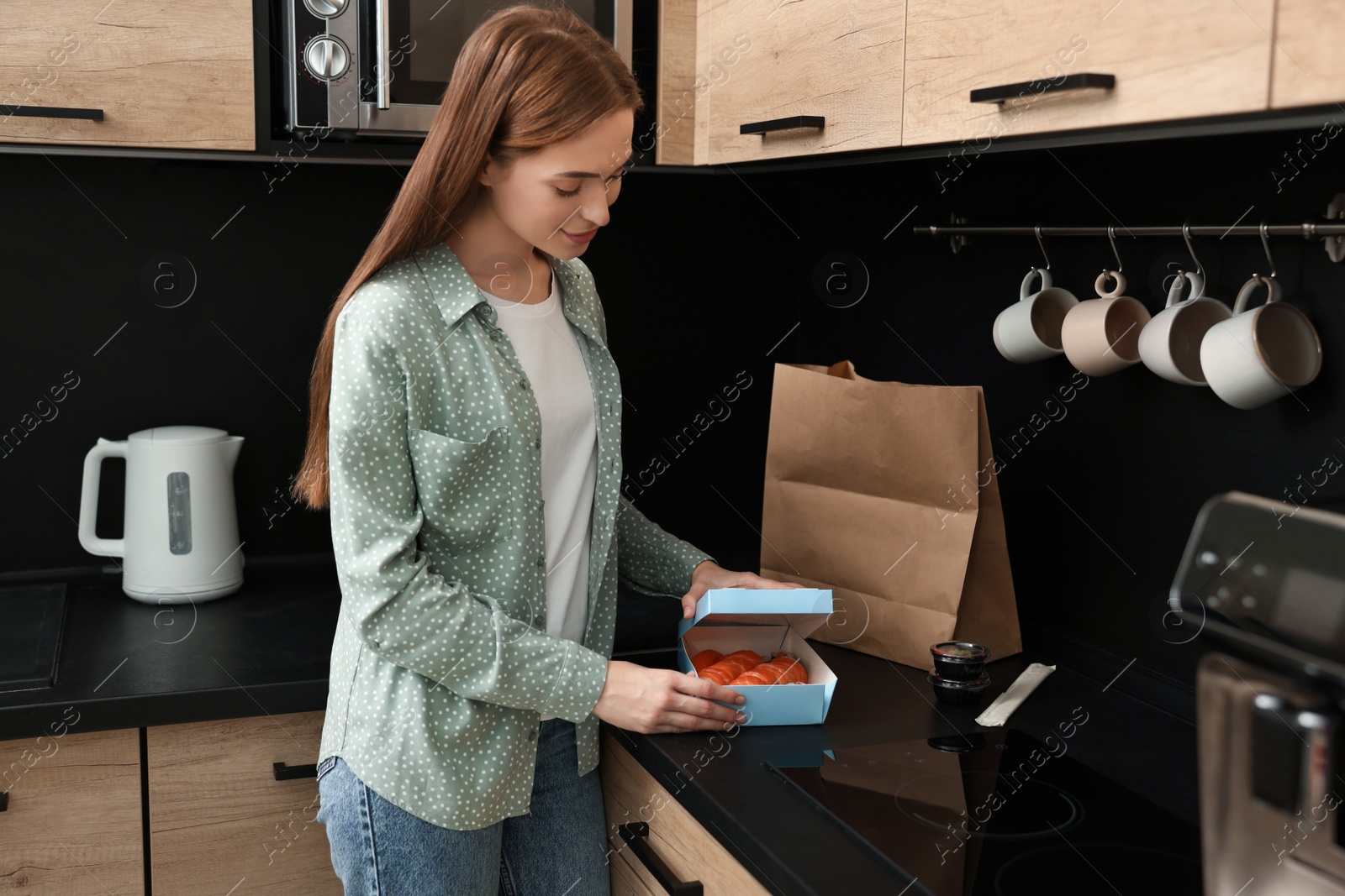 Photo of Beautiful young woman unpacking her order from sushi restaurant at countertop in kitchen