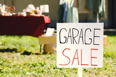 Photo of Sign Garage sale written on cardboard in yard, closeup. Space for text