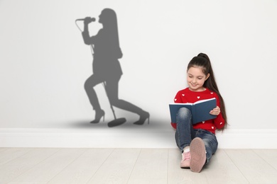 Little girl with book dreaming to be singer. Silhouette of woman behind kid's back