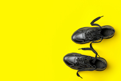 Stylish black sneakers on yellow background, flat lay. Space for text