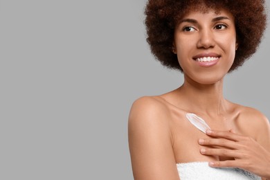 Beautiful young woman applying cream onto body on grey background, space for text