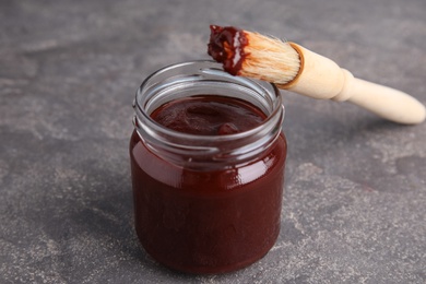 Photo of Jar with barbecue sauce and brush on grey background