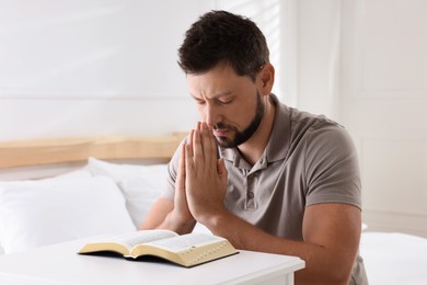 Photo of Religious man with Bible praying in bedroom