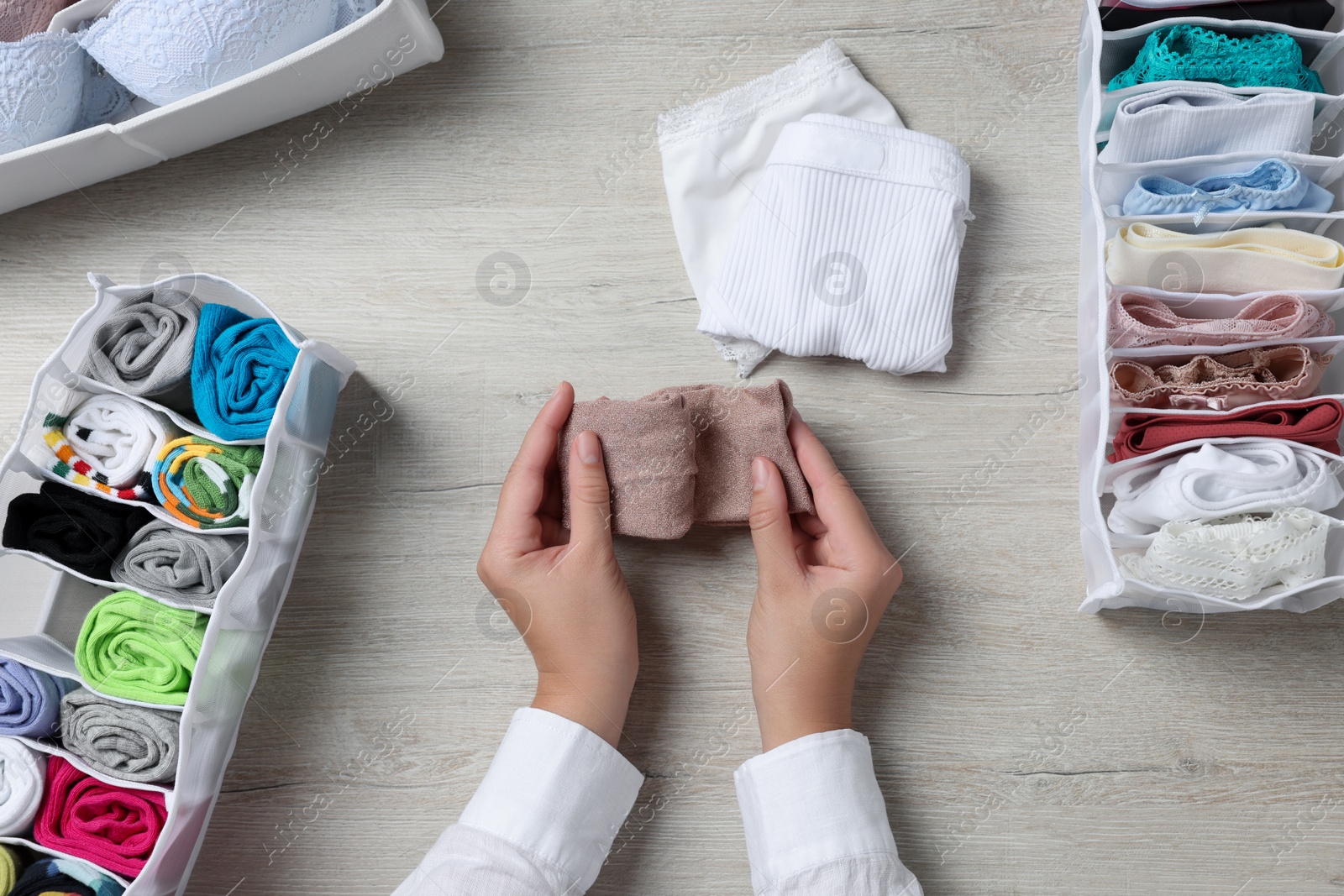 Photo of Woman rolling socks at light wooden table with organizers of underwear, top view