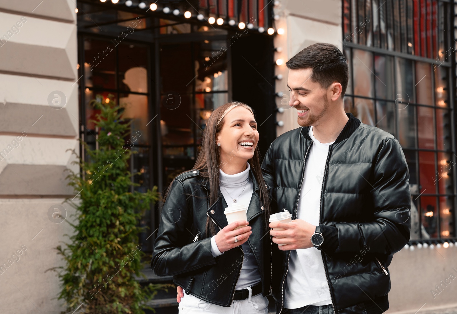 Photo of Lovely young couple with cups of coffee walking together on city street. Romantic date