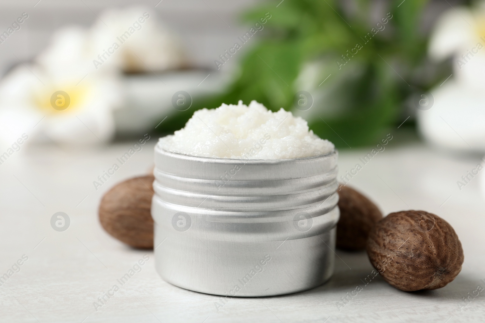 Photo of Shea butter in jar and nuts on white table, closeup