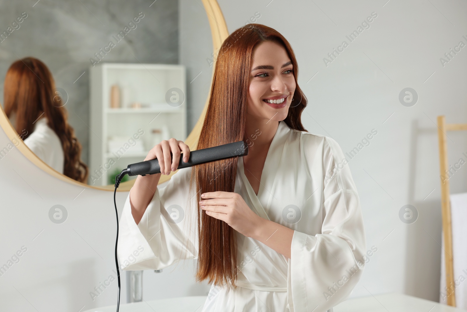 Photo of Beautiful woman using hair iron in room