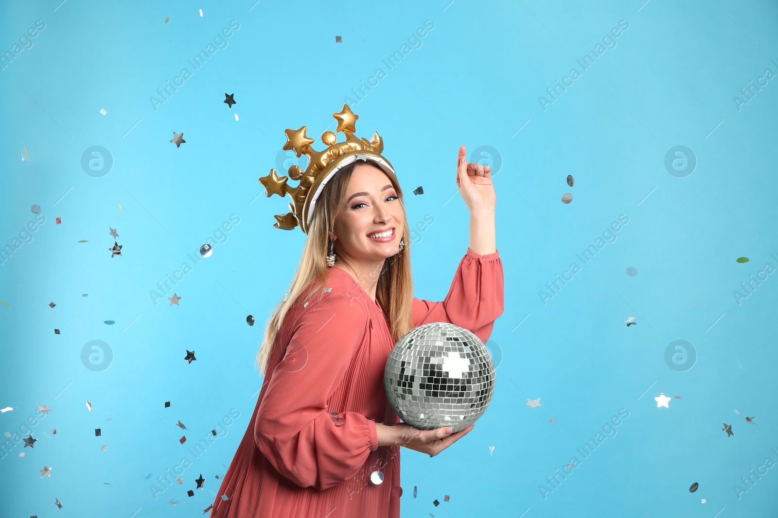 Photo of Happy young woman in party crown with disco ball and confetti on light blue background