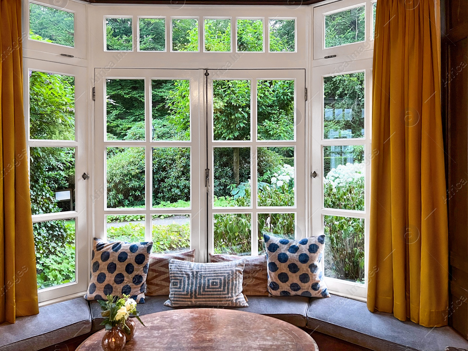 Photo of Wooden table near bay window seat with cushions in cozy room. Interior design