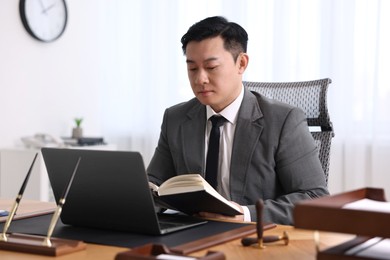 Notary working with laptop and book at wooden table in office