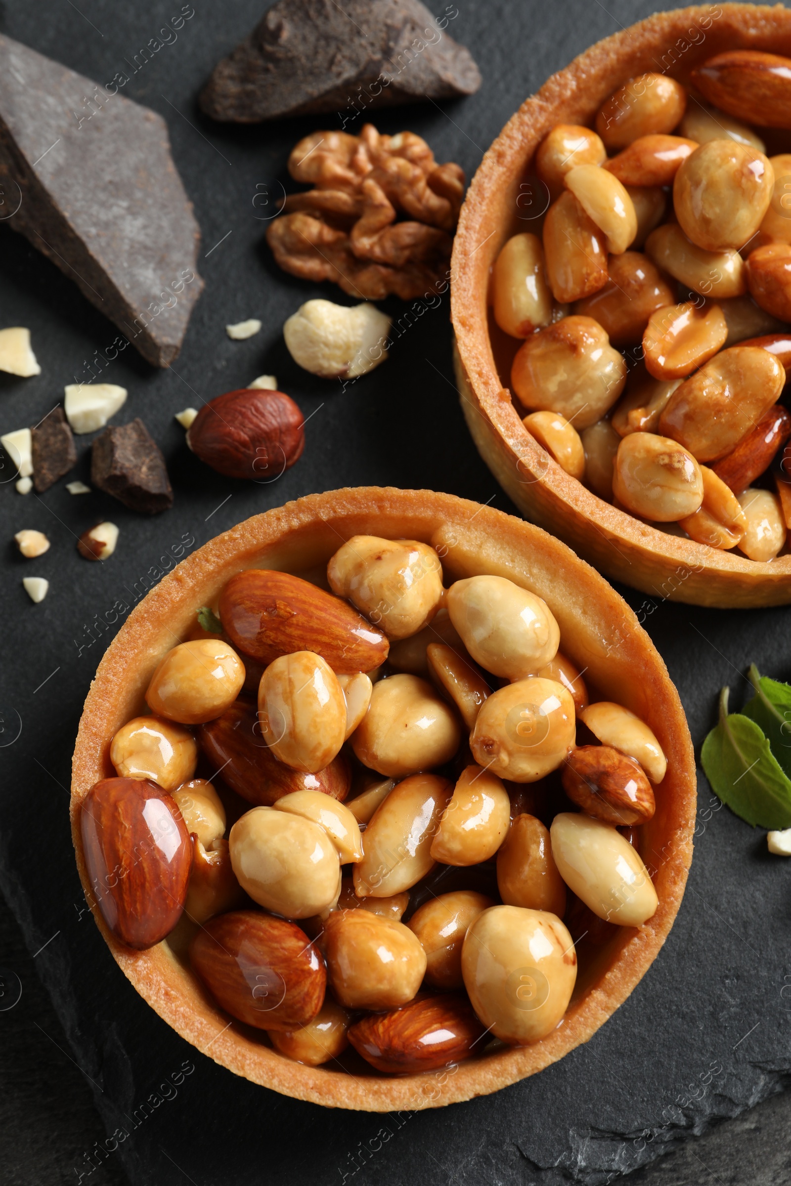 Photo of Tartlets with caramelized nuts on black table, top view. Delicious dessert