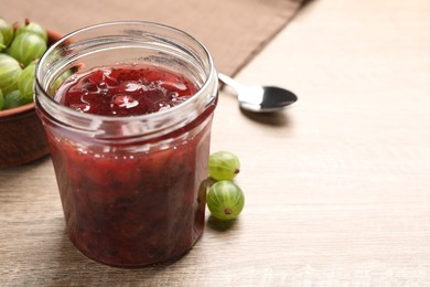Photo of Jar of delicious gooseberry jam and fresh berries on wooden table, closeup. Space for text