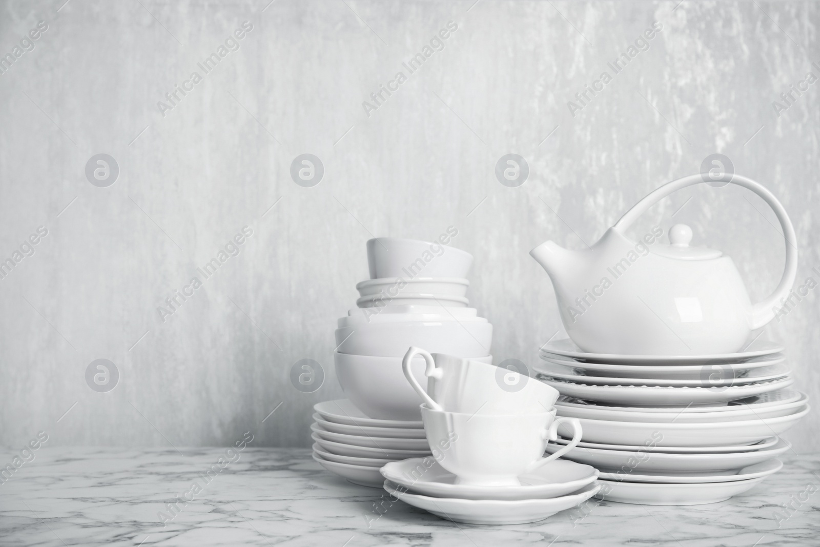Photo of Set of clean tableware on white marble table. Space for text
