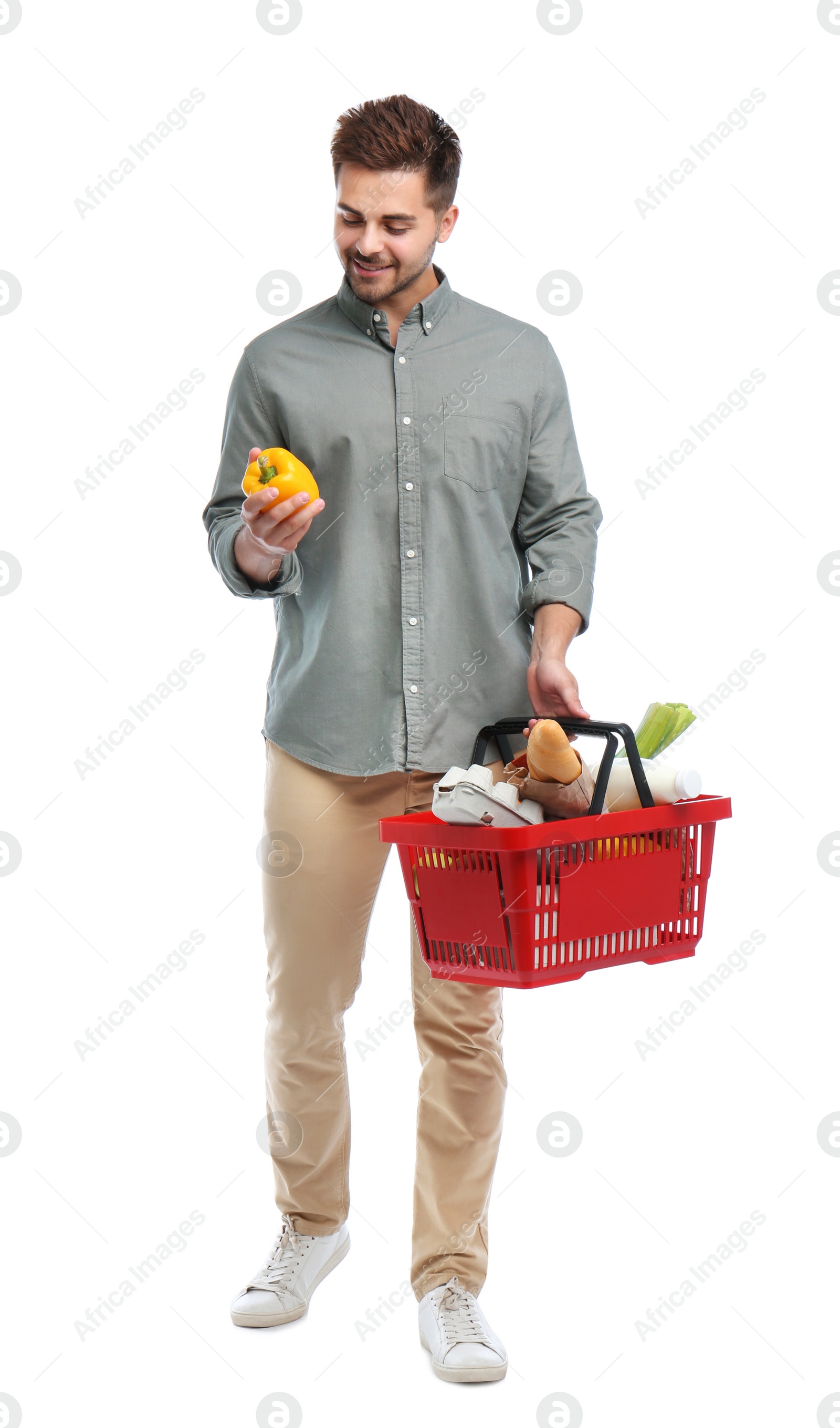 Photo of Young man with bell pepper and shopping basket full of products isolated on white
