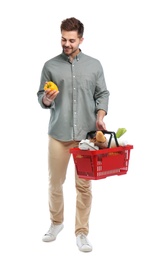 Young man with bell pepper and shopping basket full of products isolated on white