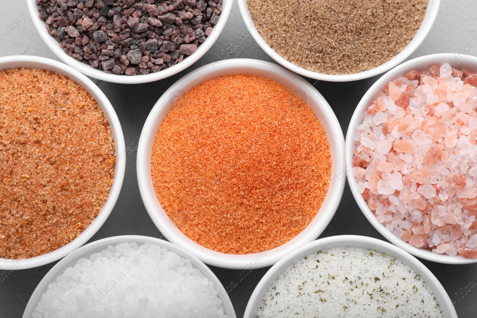 Photo of Different kinds of salt on light grey table, flat lay