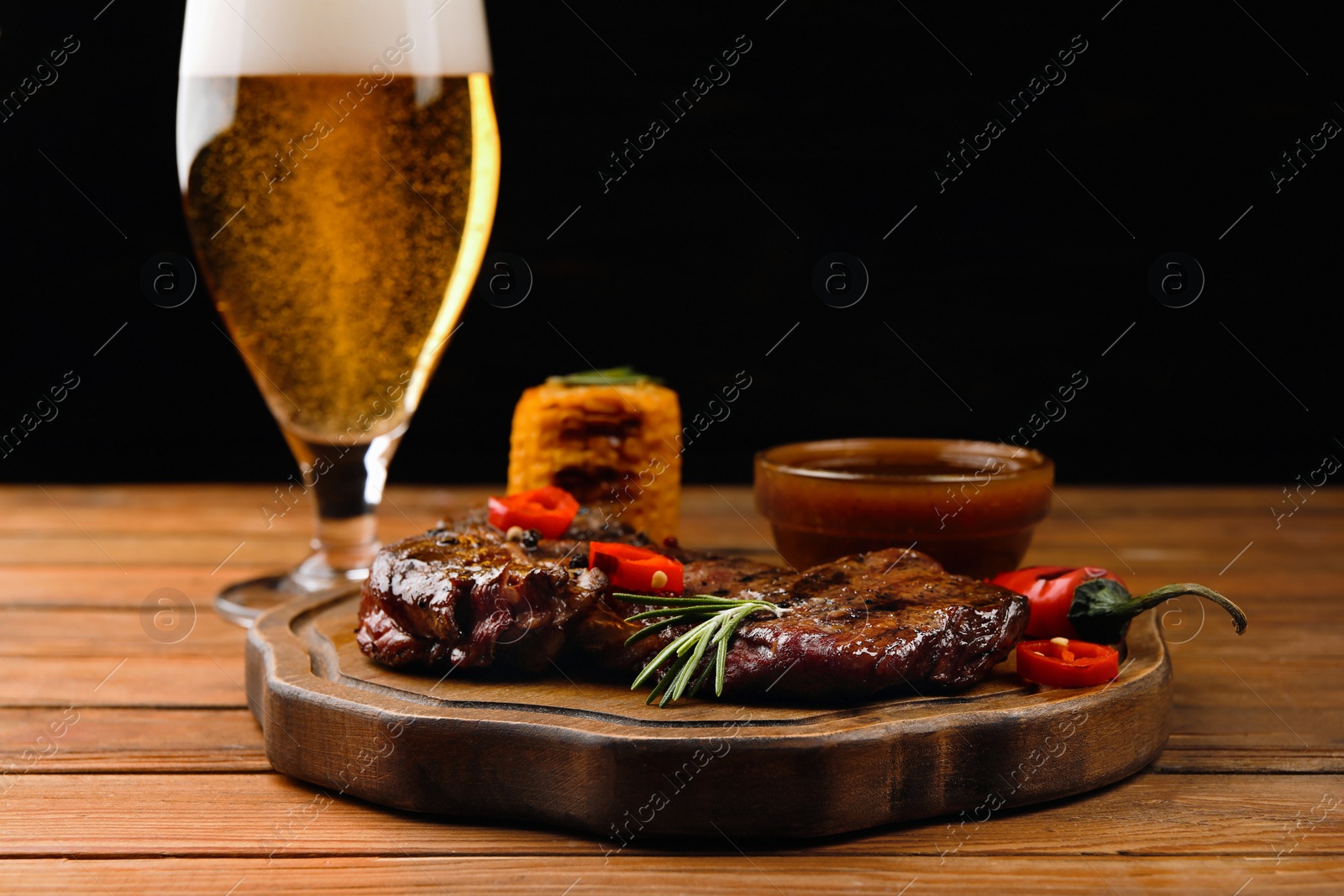 Photo of Glass of beer, delicious fried steak and sauce on wooden table