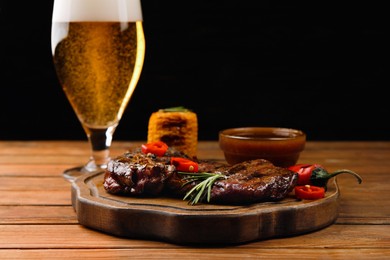 Photo of Glass of beer, delicious fried steak and sauce on wooden table