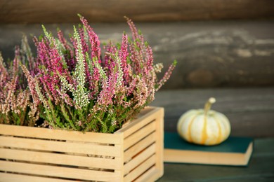 Photo of Beautiful heather flowers in crate on table near wooden wall, selective focus. Space for text