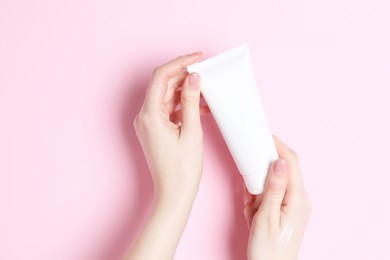 Photo of Woman holding tube of cream on pink background, closeup