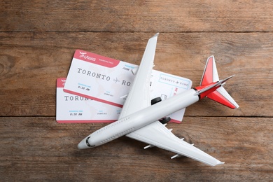 Photo of Toy airplane with tickets on wooden background, flat lay
