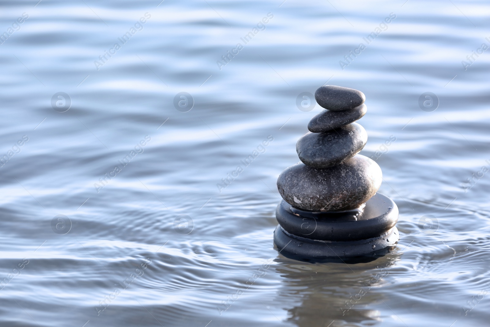 Photo of Stack of dark stones in sea water, space for text. Zen concept