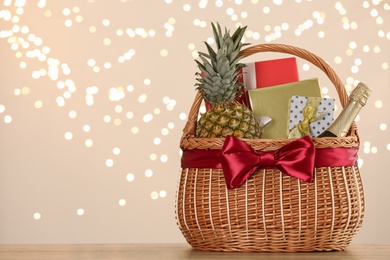 Photo of Wicker basket with gifts, champagne and food against blurred festive lights. Space for text
