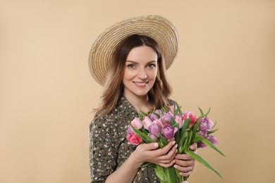 Photo of Happy young woman in straw hat holding bouquet of beautiful tulips on beige background