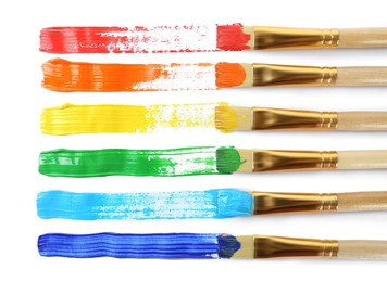 Photo of Brushes with colorful paints and strokes on white background, top view