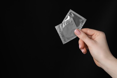 Photo of Woman holding condoms on black background, closeup. Space for text