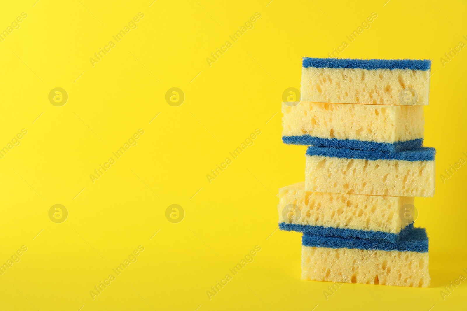 Photo of Stacked cleaning sponges on yellow background. Space for text