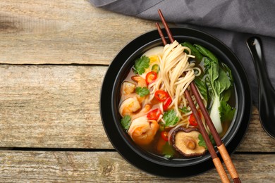 Delicious ramen with shrimps in bowl served on wooden table, top view with space for text. Noodle soup