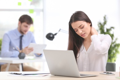 Photo of Young woman suffering from neck pain in office