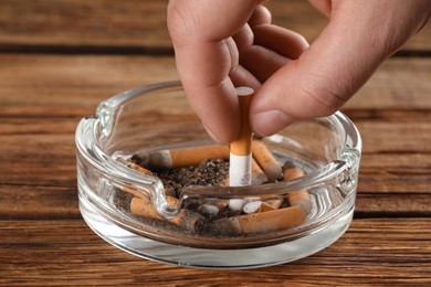 Photo of Man putting out cigarette in ashtray on wooden table, closeup