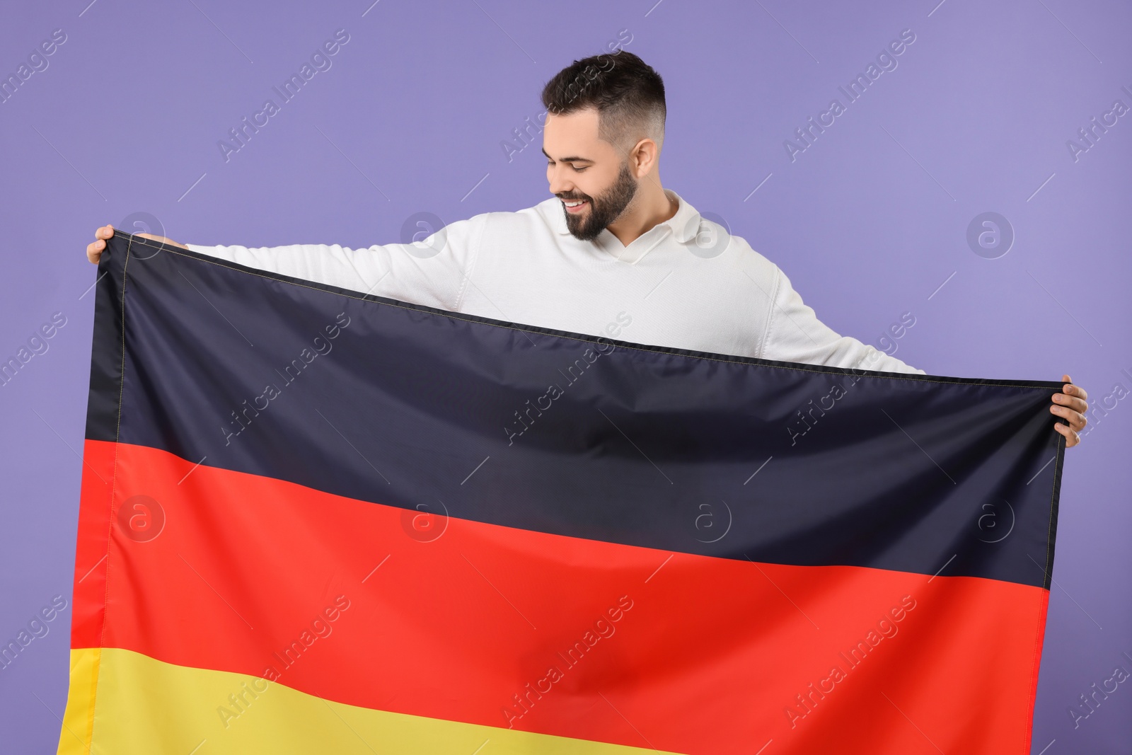 Photo of Young man holding flag of Germany on purple background