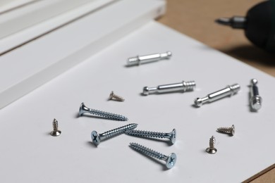 White furniture assembly parts and different metal fasteners on brown background, closeup