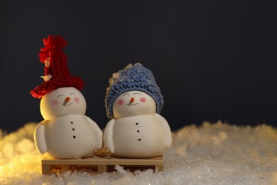 Photo of Cute decorative snowmen on artificial snow against dark background. Space for text