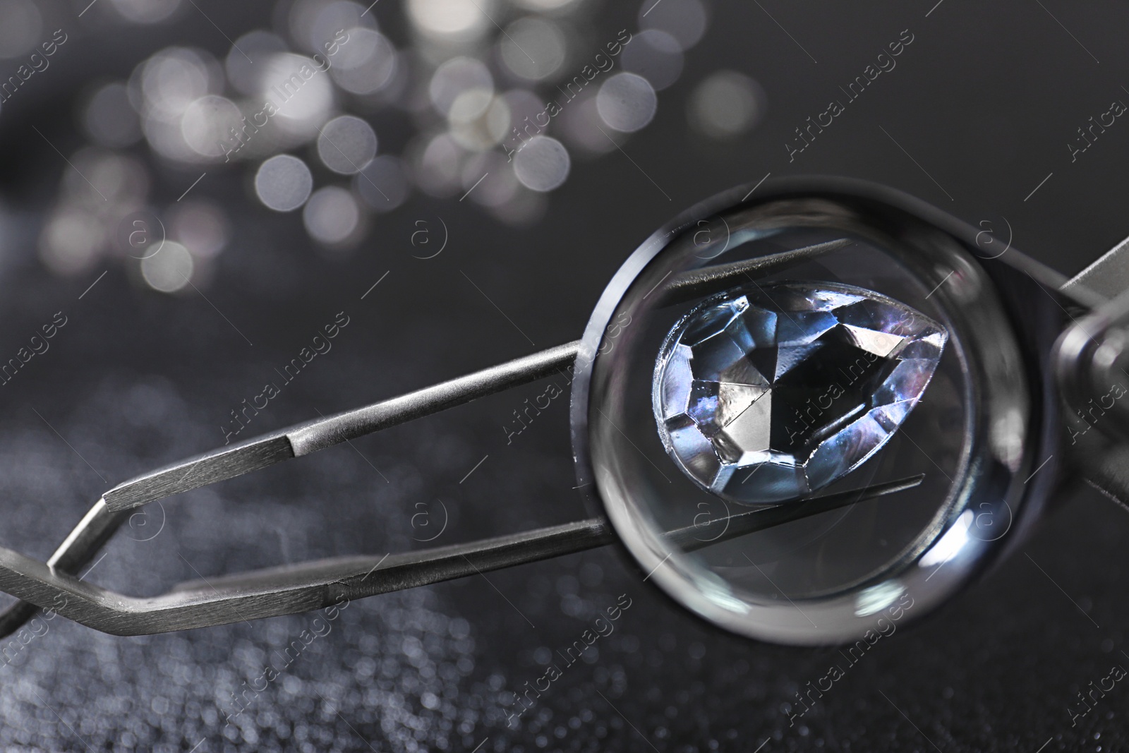 Photo of Tweezers with precious jewel over table, view through magnifier