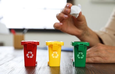 Woman throwing paper into mini recycling bin at office, closeup