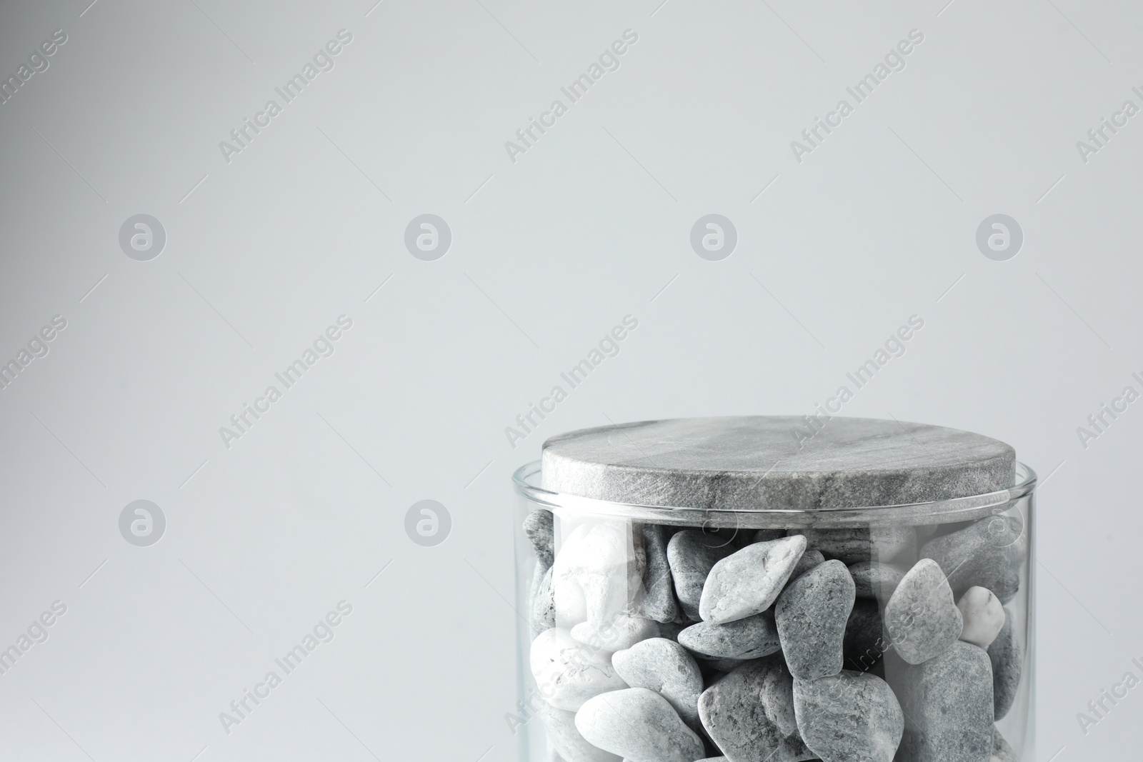 Photo of Presentation for product. Glass container with stones on light grey background. Space for text