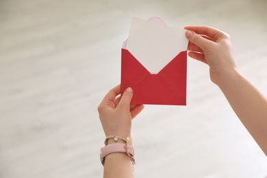 Photo of Woman holding envelope with blank greeting card against light background, closeup. Space for text