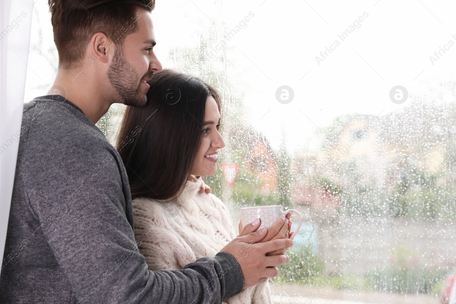 Photo of Happy young couple near window indoors on rainy day