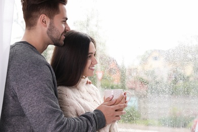 Happy young couple near window indoors on rainy day