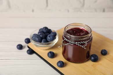 Photo of Jar of delicious blueberry jam and fresh berries on white wooden table