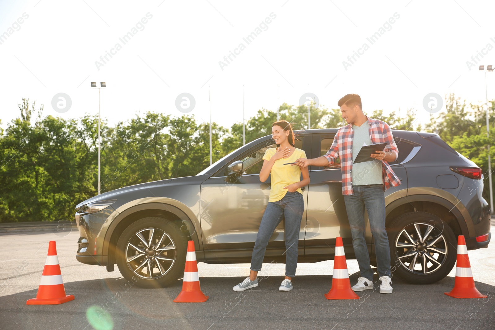 Photo of Instructor with clipboard and his student near car outdoors. Driving school exam