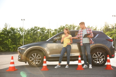 Instructor with clipboard and his student near car outdoors. Driving school exam