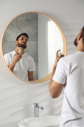 Man spraying luxury perfume near mirror indoors