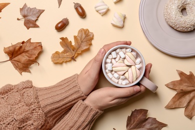 Photo of Woman in autumn sweater holding hot cozy drink on color background, top view
